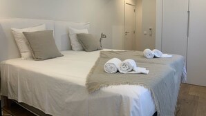 Un lit bien fait, avec des draps blancs et deux serviettes enroulées posées sur une couverture beige.