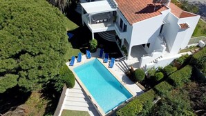 Une maison moderne à deux étages avec une piscine, entourée de verdure.