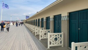 A boardwalk with rows of doors and benches, leading to a building with a tiled border.