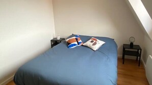 A bedroom with a bed, a nightstand, a small table, and a wall-mounted light fixture.