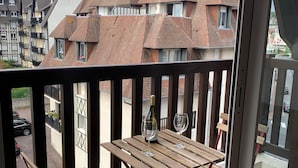 A balcony with a wooden table and chairs, a bottle of wine, and a view of residential buildings.