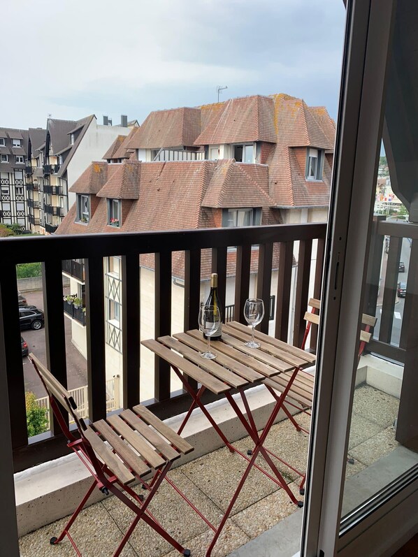 A balcony with a wooden table and chairs, a bottle of wine, and a view of residential buildings.