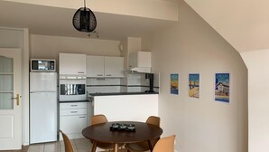A modern kitchen with white cabinets, a microwave, and a stove. There is a dining table with four chairs and a hanging light fixture.