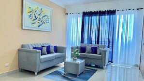 A modern living room with two grey sofas, a glass coffee table, and a large abstract painting on the wall. - Apartment with 2BD, closed to the beach, Romana Airport & Altos de Chavón.  (La Romana)