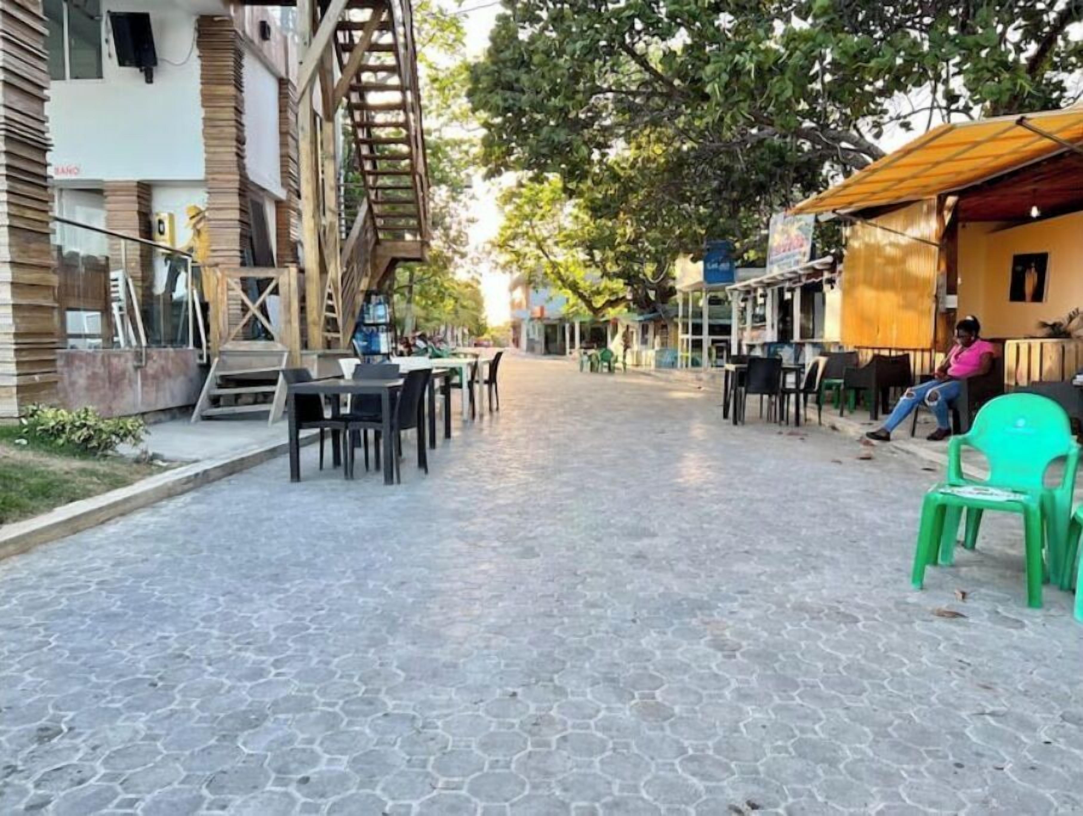 Un patio empedrado con mesas al aire libre, una escalera y edificios con balcones.