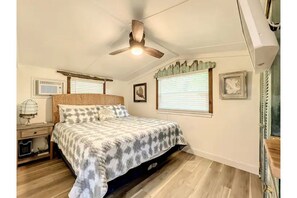 A bedroom with a bed, ceiling fan, air conditioning unit, and a window with blinds.