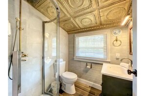 A bathroom with a glass shower enclosure, a toilet, a sink, and a window with blinds.
