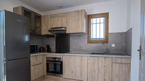 A modern kitchen with wooden cabinets, a stainless steel refrigerator, a built-in oven, and a window above the sink.