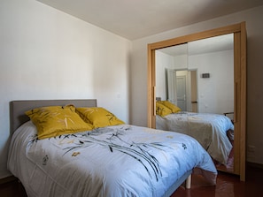 A bedroom with two beds, each with a distinct floral bedspread and a mirror on the wall.