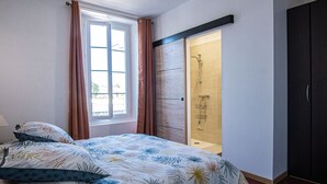 A bedroom with a bed, a window, a shower, and a wardrobe.