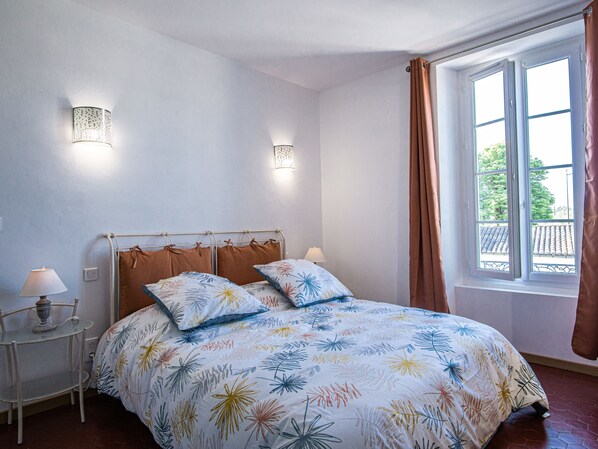 Ein Schlafzimmer mit einem Bett, zwei Wandleuchten, einem Fenster mit Vorhängen und einem kleinen Tisch mit einer Lampe.