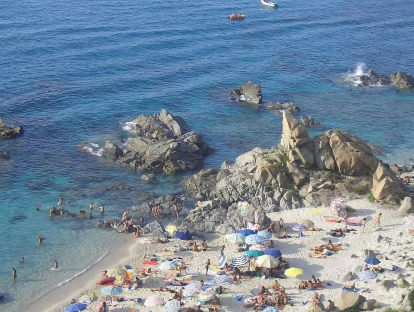 Une plage avec une eau cristalline, des formations rocheuses et des parasols.
