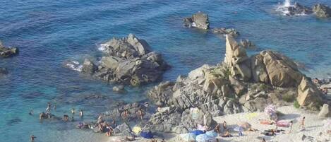 Une plage avec une eau cristalline, des formations rocheuses et des parasols.