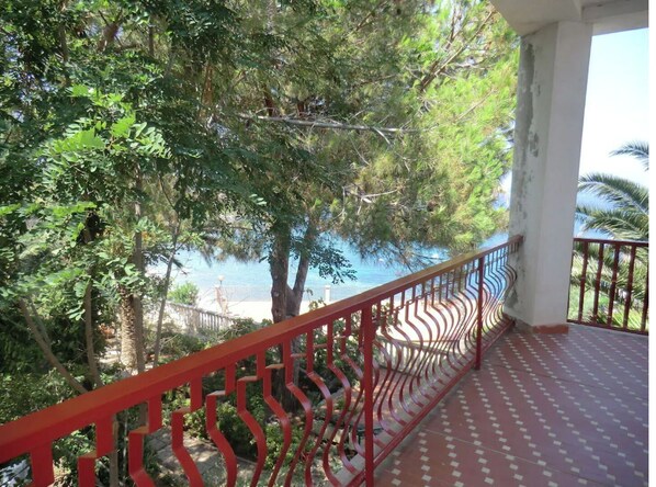 A balcony with a red railing overlooking a lush green area and a body of water.