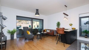 A modern living room with a sofa, chairs, a coffee table, and a kitchen area with a bar. - Hedera Estate, Hedera A15 (Dubrovnik)
