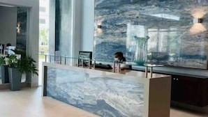 A modern reception area with a marble wall, a glass partition, and a seating area with a bench and a vase. - 🏝🏝Best View, Pool, Jacuzzi, Gym, WiFi, BBQ, Parking 🏝🏝 (Playa Juan Dolio)