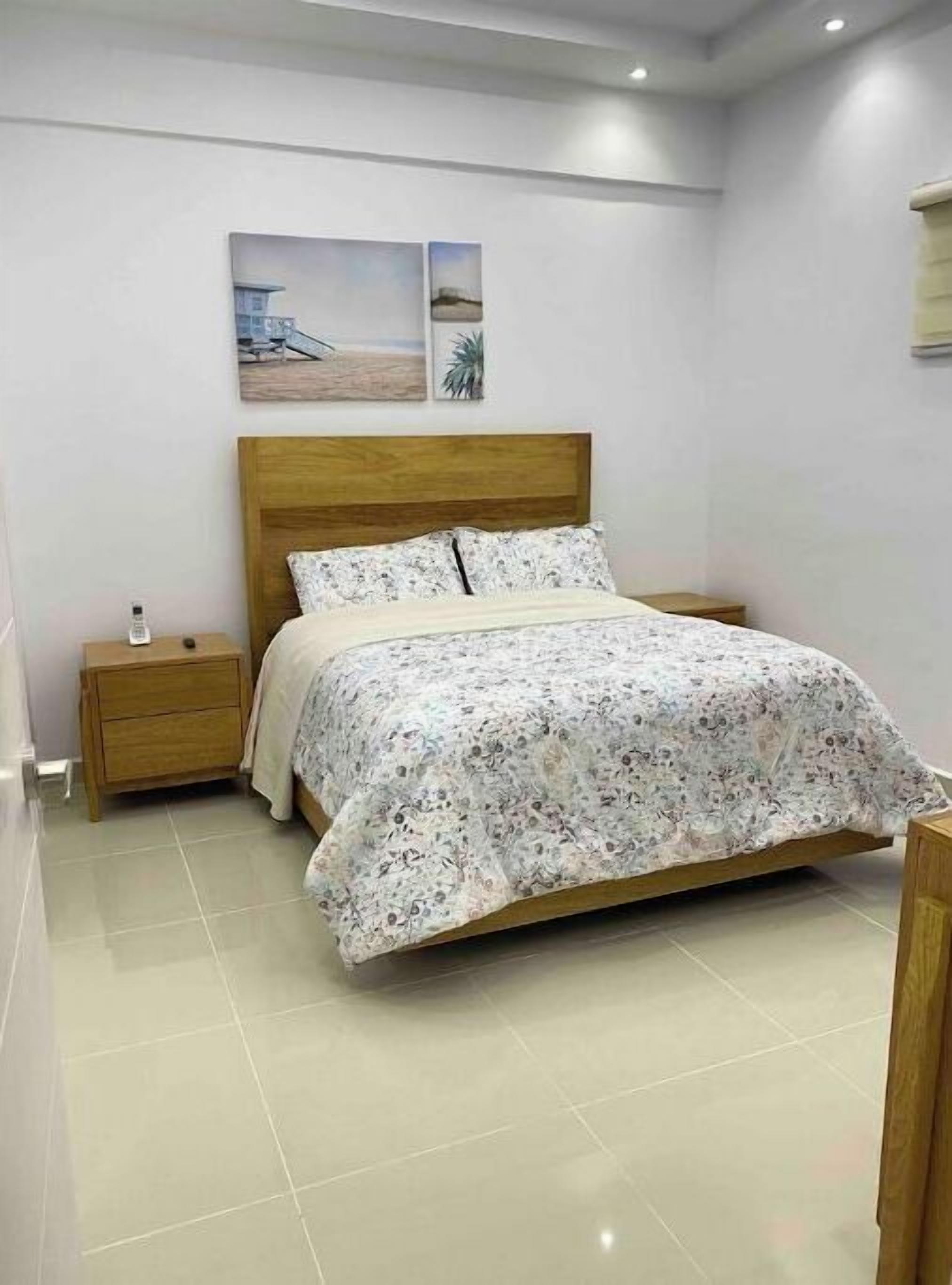 Ein ordentlich eingerichtetes Schlafzimmer mit einem hölzernen Bett, einem Nachttisch und zwei an der Wand hängenden Bildern.