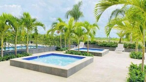 A rooftop pool area with two square hot tubs, surrounded by palm trees and lounge chairs. - 🏝🏝Best View, Pool, Jacuzzi, Gym, WiFi, BBQ, Parking 🏝🏝 (Playa Juan Dolio)
