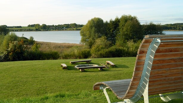 A grassy area with picnic tables and a wooden bench overlooking a lake. - Apartment "Storage apartment" (Klein Upahl)
