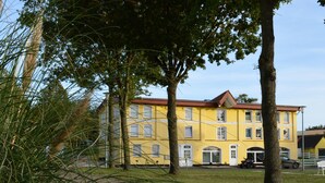 A yellow building with multiple windows and a red roof, surrounded by trees and a paved area. - Apartment "Storage apartment" (Klein Upahl)