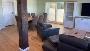 A spacious living room with a wooden floor, a large wooden pillar, a dining area with a table and chairs, a sofa set, and a TV on a white cabinet. - Apartment "Storage apartment" (Klein Upahl)