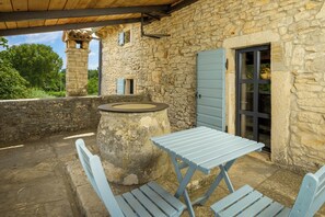 Un bâtiment en pierre surmonté d’un toit en bois, une structure circulaire en pierre et une table avec des bancs.