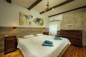 Une chambre avec un grand lit, une tête de lit en bois, une carte du monde accrochée au mur, un mur en pierre et un lustre.