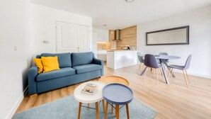 A modern living room with a sofa, coffee table, and dining area. - Cosy Appt with Terrace 5 min. DISNEYLAND (Montévrain)