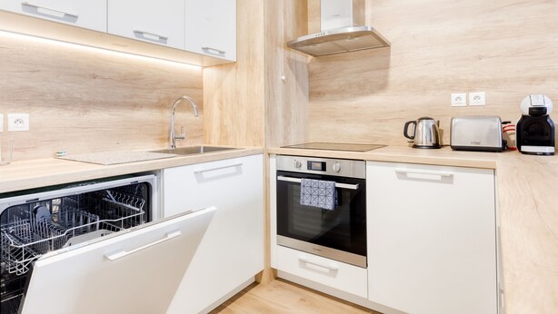 A modern kitchen with white cabinetry, a dishwasher, an oven, and a coffee maker. - Cosy Appt with Terrace 5 min. DISNEYLAND (Montévrain)