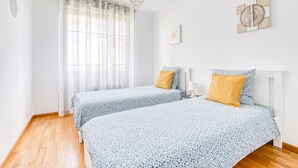 A bedroom with two beds, a window with sheer curtains, a hanging light fixture, and a wall-mounted artwork. - Cosy Appt with Terrace 5 min. DISNEYLAND (Montévrain)