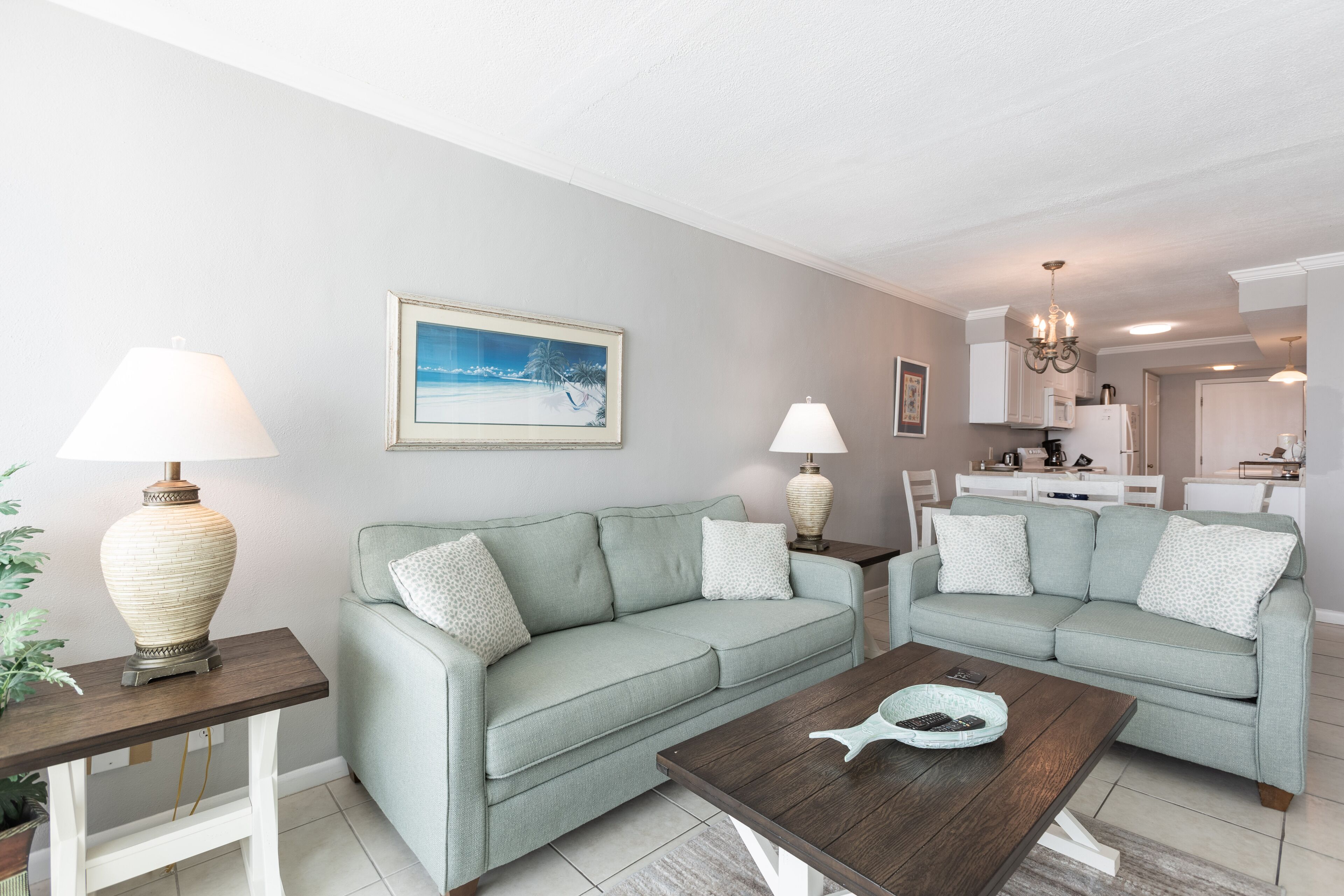 A living room with two light green sofas, a wooden coffee table, and a painting on the wall.