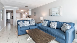 A modern living room with a blue sofa set, a wooden coffee table, and a kitchen in the background. - IS655- *Labor Day Special!*  Beach Front, Park & Walk! Look at This View! (Gulf Shores)