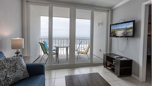 A living room with a sofa, a TV mounted on the wall, a dining table with chairs, and a view through a sliding glass door to the outside. - IS655- *Labor Day Special!*  Beach Front, Park & Walk! Look at This View! (Gulf Shores)