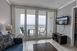 Relax in this stylish living room with a sofa, coffee table, and TV, offering a view of the beach through large glass doors.