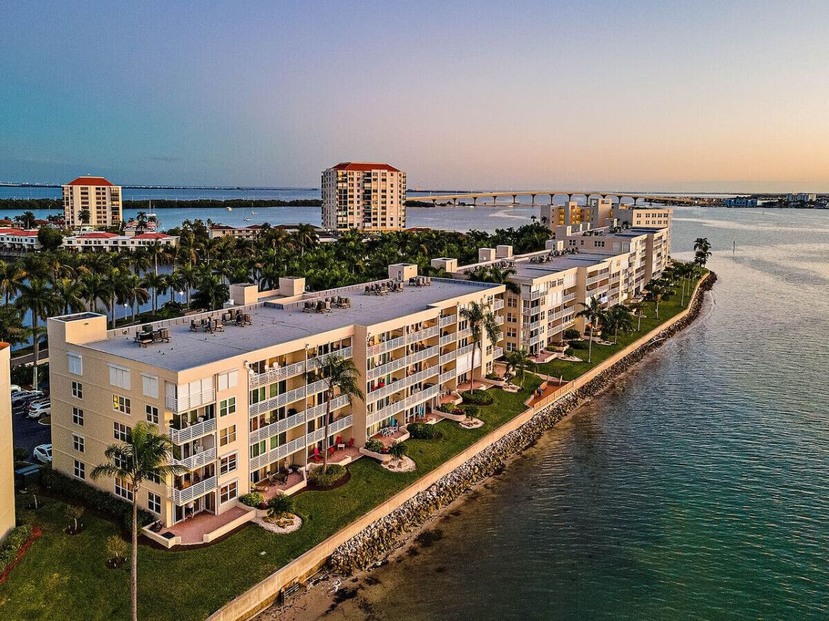 A beachfront hotel with multiple buildings, a long promenade, and a bridge in the background.