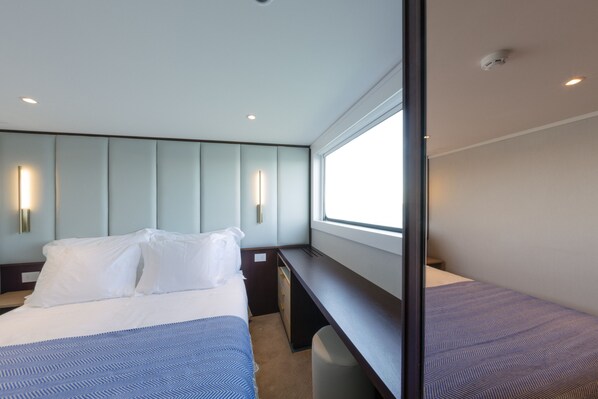 Une chambre d’hôtel équipée d’un lit, de tables de chevet, d’une fenêtre et d’un éclairage fixé au mur.