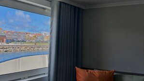 Une pièce avec vue sur le bord de l’eau, un canapé avec des coussins et une fenêtre avec des rideaux.