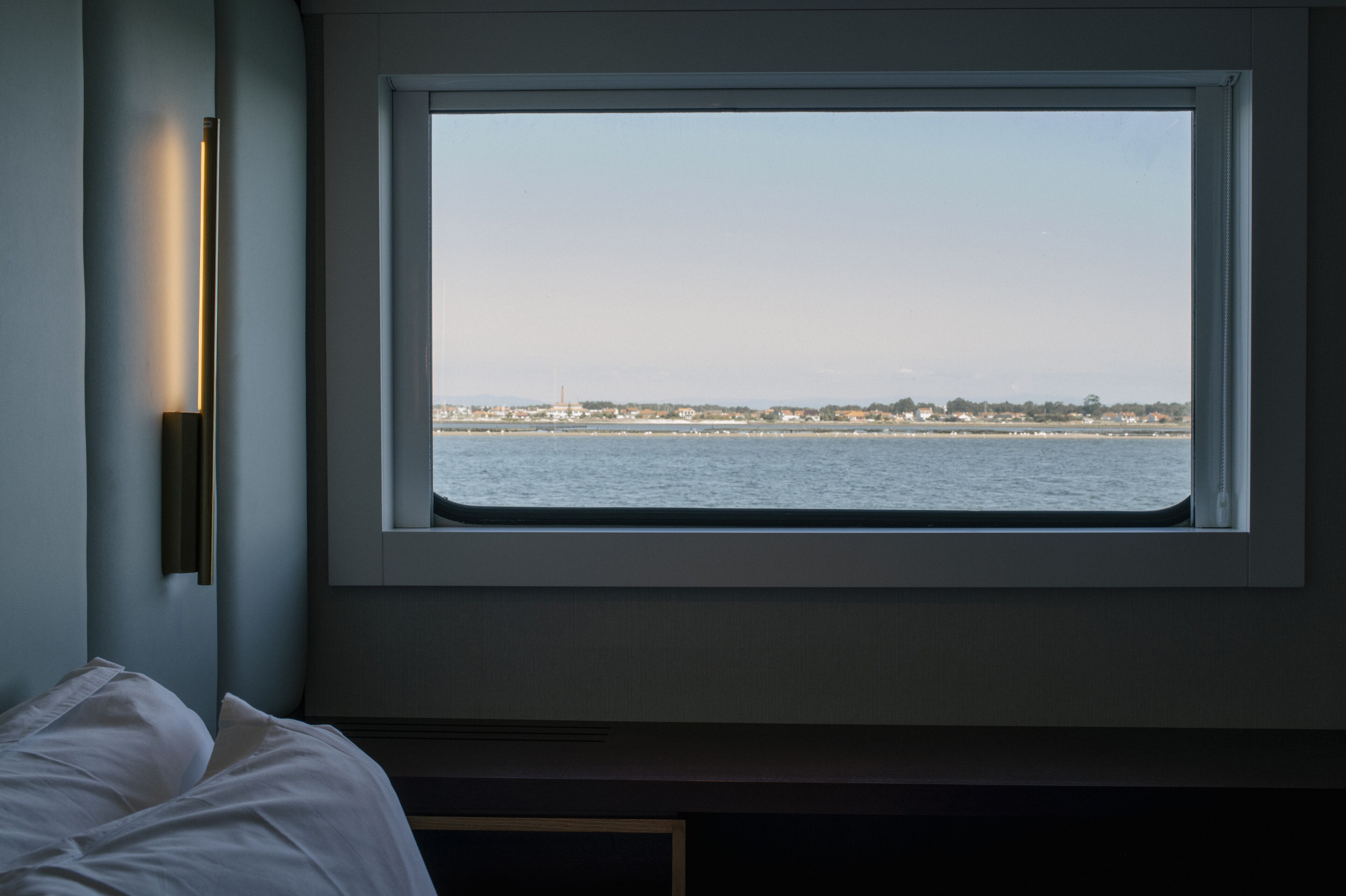 Ein Zimmer mit großem Fenster mit Blick auf ein Gewässer und eine entfernte Küste.
