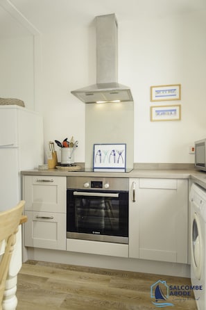 Une cuisine moderne avec des meubles blancs, un four Bosch, une hotte en acier inoxydable et un lave-linge.
