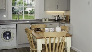 Una cocina moderna con una mesa de comedor de madera, sillas, una lavadora y una ventana con vistas a la vegetación.