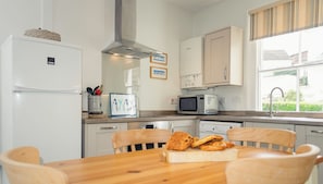 A kitchen with a wooden table, chairs, a refrigerator, microwave, and a window with a view.