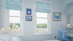 A bedroom with two windows, a bed, a chair, and a lamp.