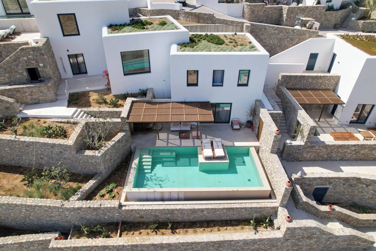 A modern villa with a rooftop pool, stone walls, and a flat roof garden.