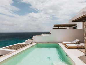 Una piscina con vista al océano, un edificio blanco y un muro de piedra.