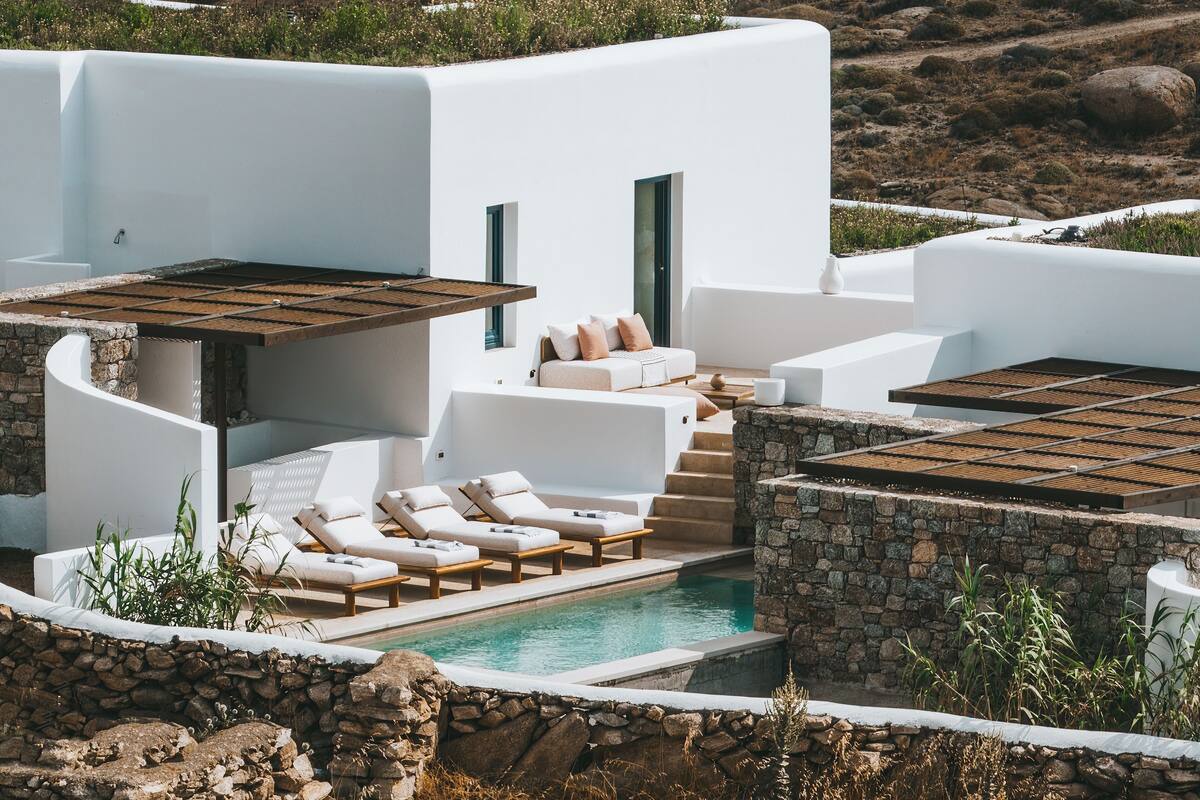 A modern white building with a pool, sun loungers, and a stone wall.