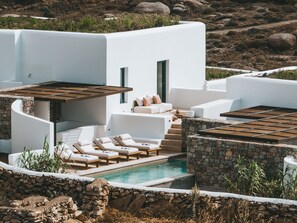 Un edificio moderno blanco con piscina, tumbonas y una pared de piedra.