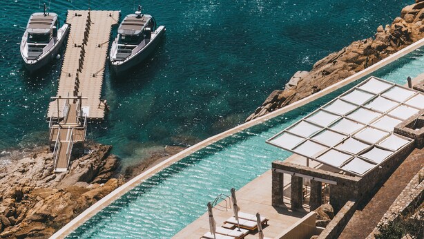 A pier with boats docked, a swimming pool with sun loungers, and a stone structure. - Cali Mykonos (Mykonos)