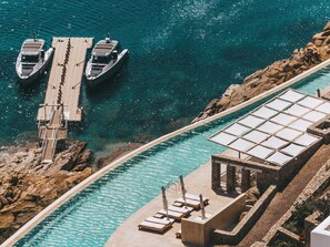 A pier with boats docked, a swimming pool with sun loungers, and a stone structure. - Cali Mykonos (Mykonos)