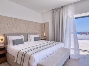 Un dormitorio moderno con una cama grande, una mesita de noche y vista al mar a través de cortinas translúcidas.