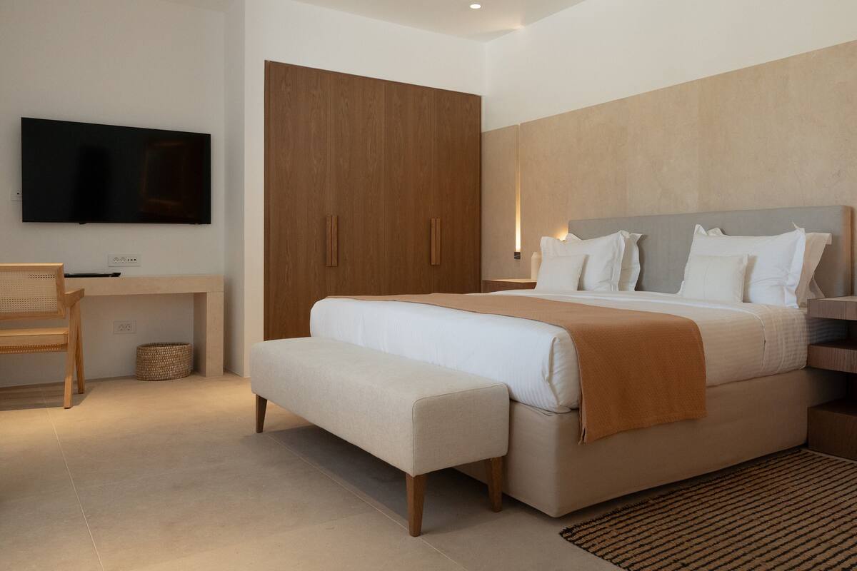 A modern bedroom with a large bed, a desk, a television, and a wardrobe.